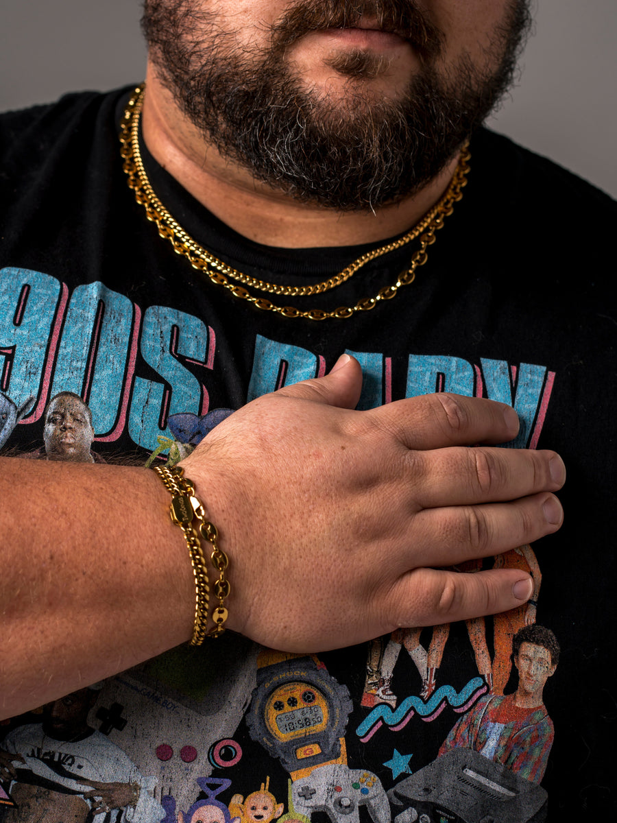 A man with his hand on his chest wearing layered Two Kxngs gold chains