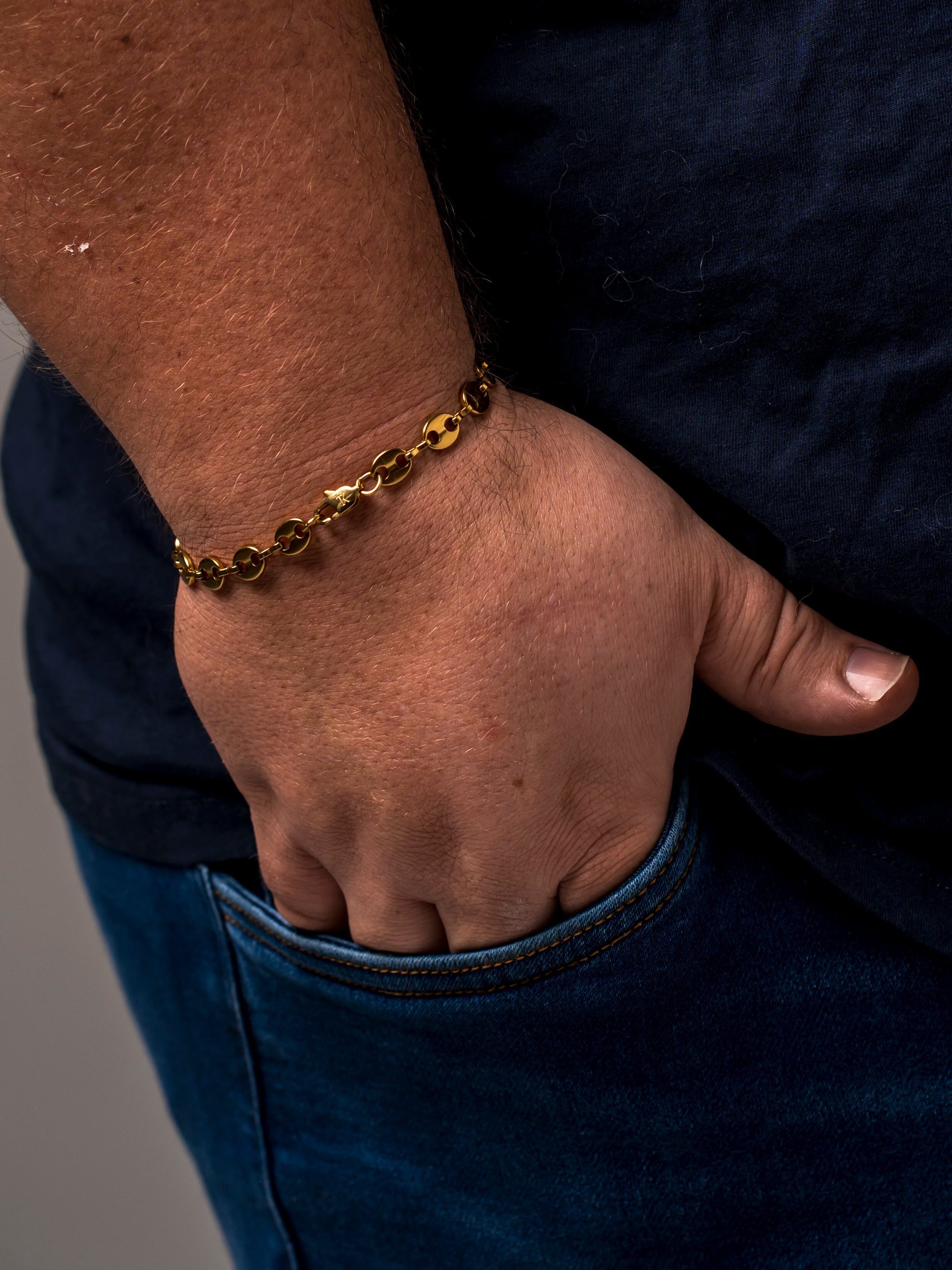 A gold Two Kxngs mariner bracelet on a man's wrist, hand in his jeans pocket