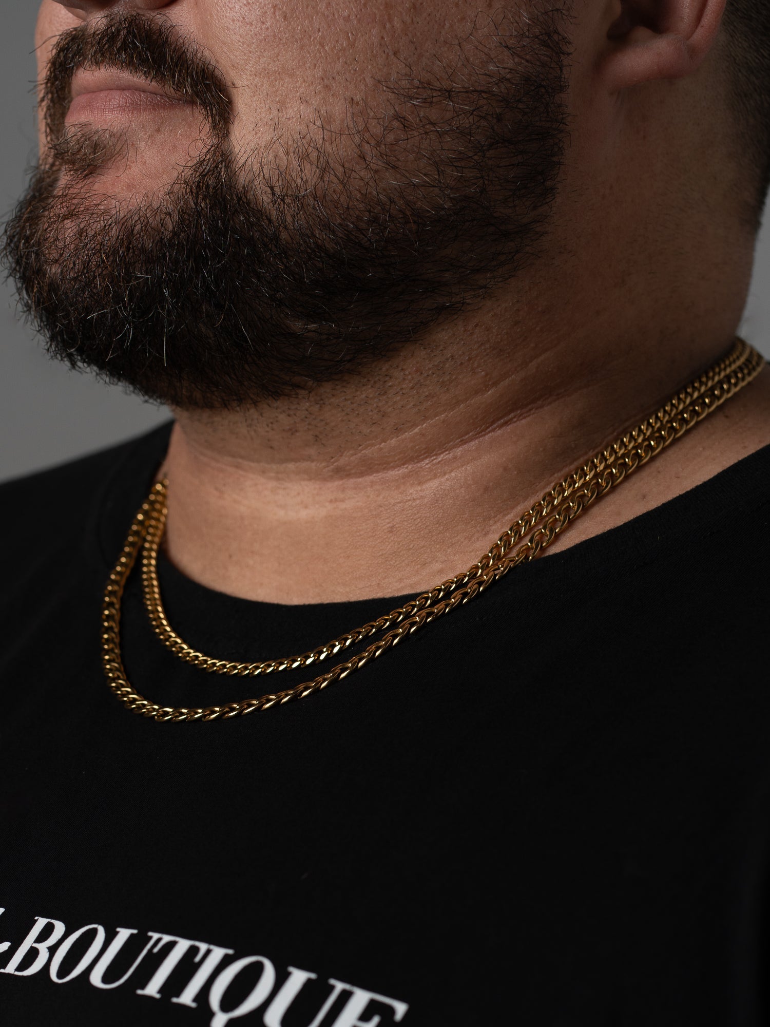 Two layered gold Two Kxngs chains worn together over a black t-shirt